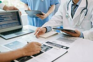 Medical team having a meeting with doctors in white lab coats and surgical scrubs seated at a table discussing a patients working online using computers in medical industry photo