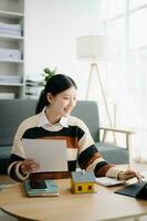 Young real estate agent worker working with laptop and tablet at table in home office and small house beside it. photo