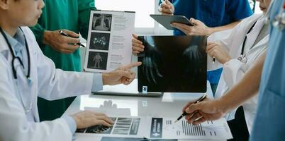 Medical team having a meeting with doctors in white lab coats and surgical scrubs seated at a table discussing a patients working online using computers in the medical industry photo