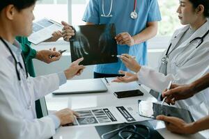 Medical team having a meeting with doctors in white lab coats and surgical scrubs seated at a table discussing a patients working online using computers in the medical industry photo