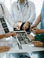 médico equipo teniendo un reunión con doctores en blanco laboratorio abrigos y quirúrgico matorrales sentado a un mesa que se discute un pacientes trabajando en línea utilizando ordenadores en el médico industria foto