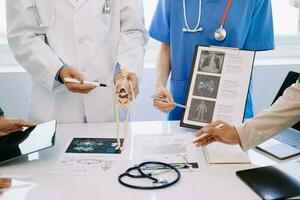 Medical team having a meeting with doctors in white lab coats and surgical scrubs seated at a desk discussing a patients working online using computers in the medical industry photo