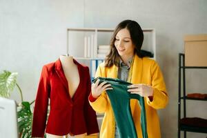 Fashion designer woman talking smart phone and using laptop with digital tablet computer in modern studio the clothes hanging on the racks photo