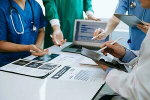 Medical team having a meeting with doctors in white lab coats and surgical scrubs seated at a table discussing a patients working online using computers in medical industry photo