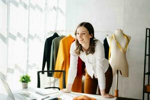 caucásico joven mujer en escritorio en hogar oficina de Moda diseñador y sostiene tableta, ordenador portátil y teléfono inteligente foto