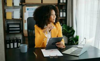 Beautiful African business woman typing laptop and tablet Placed at the table at the office photo