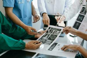 Medical team having a meeting with doctors in white lab coats and surgical scrubs seated at a table discussing a patients working online using computers in the medical industry photo