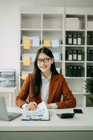 confiada hermosa mujer de negocios asiática escribiendo computadora portátil y tableta digital mientras toma café en la oficina foto