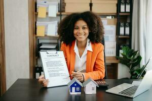 Young real estate agent worker working with laptop and tablet at table in office and small house beside it. photo