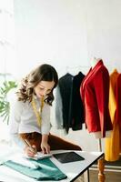 Caucasian young woman on desk in home office of fashion designer and holds tablet, laptop and smartphone. photo