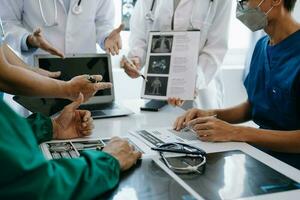 Medical team having a meeting with doctors in white lab coats and surgical scrubs seated at a table discussing a patients working online using computers in the medical industry photo