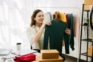 Asian tailor woman working on clothes in tailoring atelier.  beautiful young female fashion designer smile and after success in studio photo