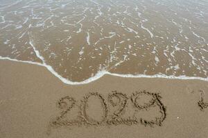 nuevo año 2029 escrito en el arena en un playa con mar ola antecedentes. foto