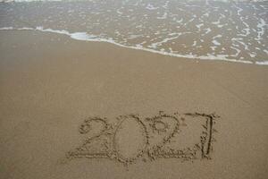 New Year 2027 written in the sand on a beach with sea wave background. photo