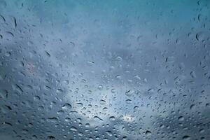 Rain drops on window glass with cloudy sky background. photo