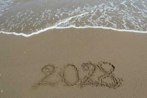 New Year 2028 written in the sand on a beach with sea wave background. photo