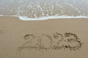 año 2023 escrito en el arena en un playa con mar ola antecedentes. foto