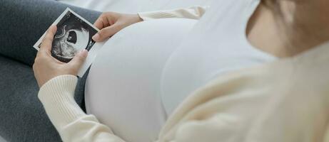 la mujer embarazada está mirando una foto de ultrasonido del feto. la madre toca suavemente al bebé en el estómago. feliz, familia, crecimiento, embarazo, disfrute, preparar recien nacido, cuidar, salud, pancita.