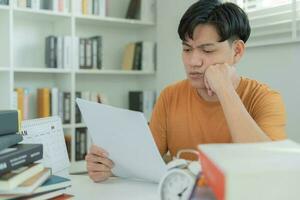 Asian student man have anxiety because of exams, male prepare for test and learning lessons in the library. stress, despair, haste, misunderstanding reading, discouraged, expectation, knowledge, tired photo