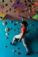 mujer alpinismo en pared formación en gimnasia, activo deportivo hembra practicando rock alpinismo en artificial rock en extremo deporte, búlder, muro, trepador es capacitación, rock alpinismo en el ciudad, fuerte foto