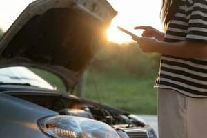 breakdown, broken car, repair. Woman uses mobile phone check insurance premiums through application due to car accident . Find garage to get car fixed during country tour, waiting for help, emergency. photo