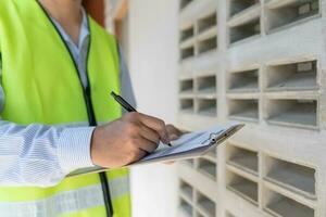 inspector or engineer is inspecting construction house using a checklist. Engineers and architects or contactor count materials for construction. Building, check, insurance house, quality, foreman. photo