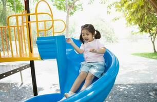 Cute asian girl smile play on school or kindergarten yard or playground. Healthy summer activity for children. Little asian girl climbing outdoors at playground. Child playing on outdoor playground. photo