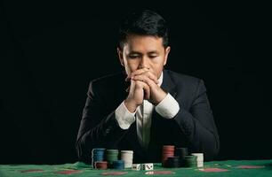 Asian man dealer or croupier shuffles poker cards betting in casino on black background of green table, Dealer man invitation bet playing cards. Casino, poker, poker game concept. photo