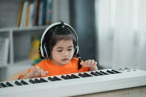 Asian cute girl wearing headphone learning online piano music with teacher by mobile phone or tablet. The idea of activities for the child at home during quarantine. Music learning study concept. photo