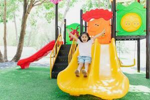 Cute asian girl smile play on school or kindergarten yard or playground. Healthy summer activity for children. Little asian girl climbing outdoors at playground. Child playing on outdoor playground. photo
