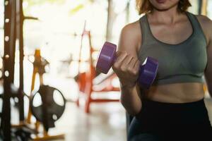 Asian fit sportswoman smiling and working out excercise weights with dumbbells at the fitness gym. asian woman wearing sportwear doing exercise to burn fat at gym. Sport woman fitness concept. photo