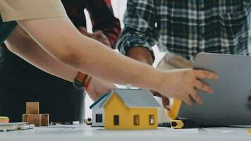 equipo de construcción trabajadores vistiendo protector cascos y chalecos que se discute proyecto detalles con ejecutivo supervisor en pie a mesa con planos, herramientas y ordenador portátil en eso video