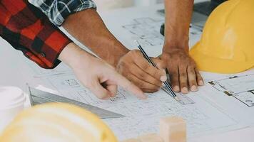 Team of construction workers wearing protective helmets and vests discussing project details with executive supervisor standing at table with blueprints, tools and laptop on it video