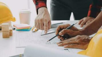 team van bouw arbeiders vervelend beschermend helmen en vesten bespreken project details met uitvoerend leidinggevende staand Bij tafel met blauwdrukken, gereedschap en laptop Aan het video