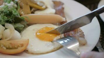mit Messer und Gabel Schneiden Ei Eigelb zu Essen gebraten Ei im Weiß Platte. Schneiden sonnig Seite oben Ei mit flüssig Ei Eigelb video