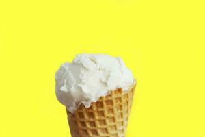 Ice cream in waffle cone close-up. Sweet summer vanille dessert over yellow background photo