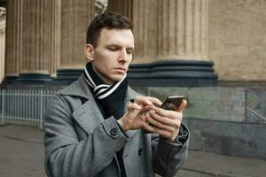 Close-up shot fashionable young man using his mobile phone, wearing man's coat photo