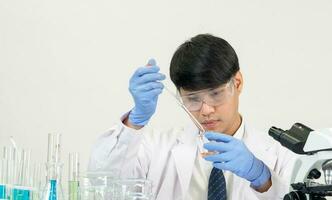 Asian male student scientist Wearing a doctor's gown in the lab looking at the chemist. caused by mixing reagents in scientific research laboratories with test tubes and microscope on the table photo