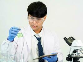 Asian male student scientist Wearing a doctor's gown in the lab looking at the chemist. caused by mixing reagents in scientific research laboratories with test tubes and microscope on the table photo