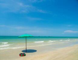 vista frontal del paisaje playa azul ola de mar con cielo fresco de vacaciones con sombrilla verde instalada en la arena para los turistas que indican que no importa cuán caliente sea el sol en verano, la pequeña sombra es valiosa, tailandia foto