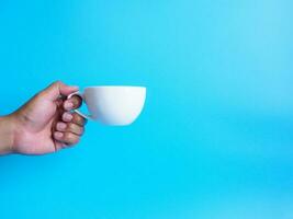 Man hand holding a white coffee cup, filled with hot black coffee americano no sugar no milk, ready to drink, refreshing. aroma awake fresh to work placed on a blue isolated background photo