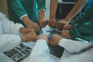 Mature doctors and young nurses stacking hands together at hospital. Close up hands of medical team stacking hands. Group of successful medical doctors and nurses stack of hands. photo