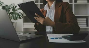 Asian Business woman using calculator and laptop for doing math finance on an office desk, tax, report, accounting, statistics, and analytical research concept photo