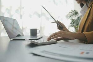 Asian Business woman using calculator and laptop for doing math finance on an office desk, tax, report, accounting, statistics, and analytical research concept photo