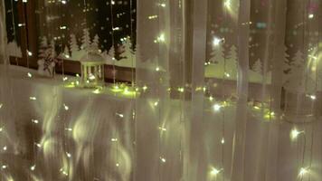 Christmas ornaments and light reflected on the window at night behind transparent curtain video
