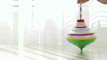 Colorful spinning top moving on a table with transparent curtain on the background. video