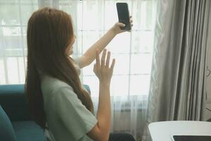 Happy Asian teen girl holding pad computer gadget using digital tablet technology sitting on the couch at home. Smiling young woman using apps, shopping online, reading news, browsing internet on sofa photo