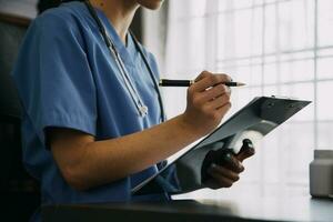 Young doctor with diary sitting at desk in medical clinic photo