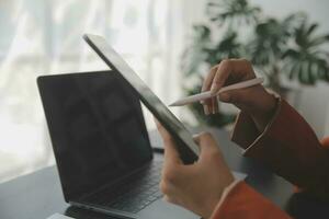 Portrait of Young Asian woman hand freelancer is working her job on computer tablet in modern office. Doing accounting analysis report real estate investment data, Financial and tax systems concept. photo