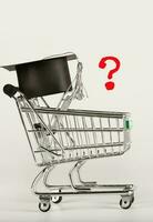 Square academic cap on a shopping cart and depicted question mark. photo